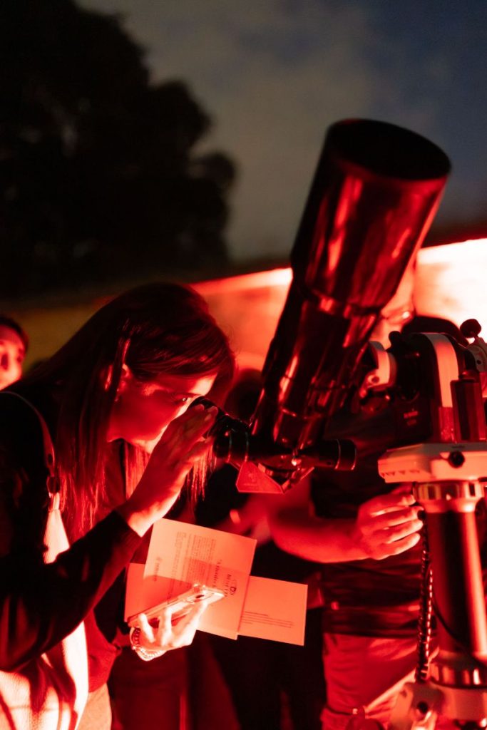 Signora con fogli in mano che osserva al telescopio